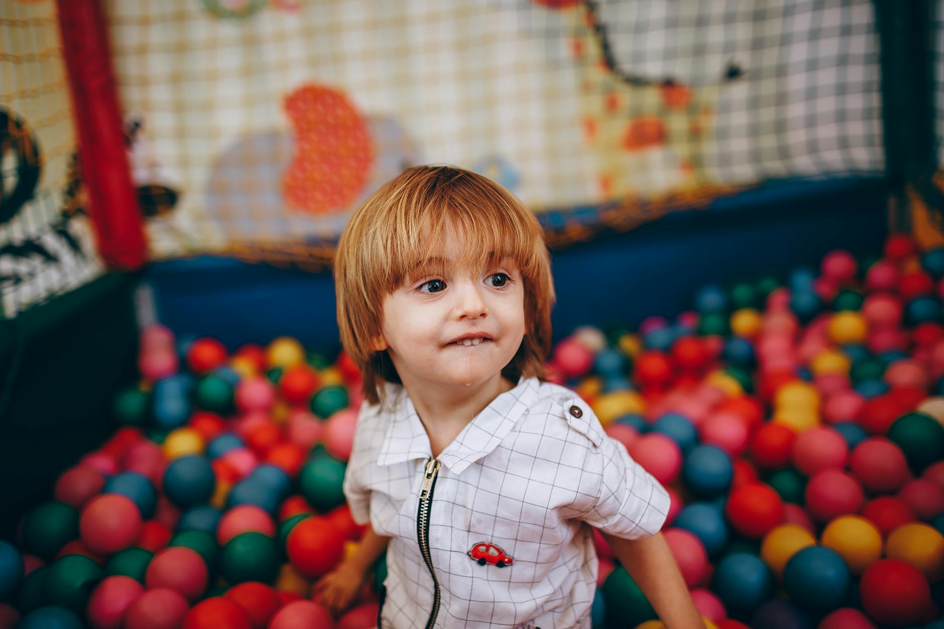 Małe dziecko bawi się w kolorowym basenie z piłkami w żłobku