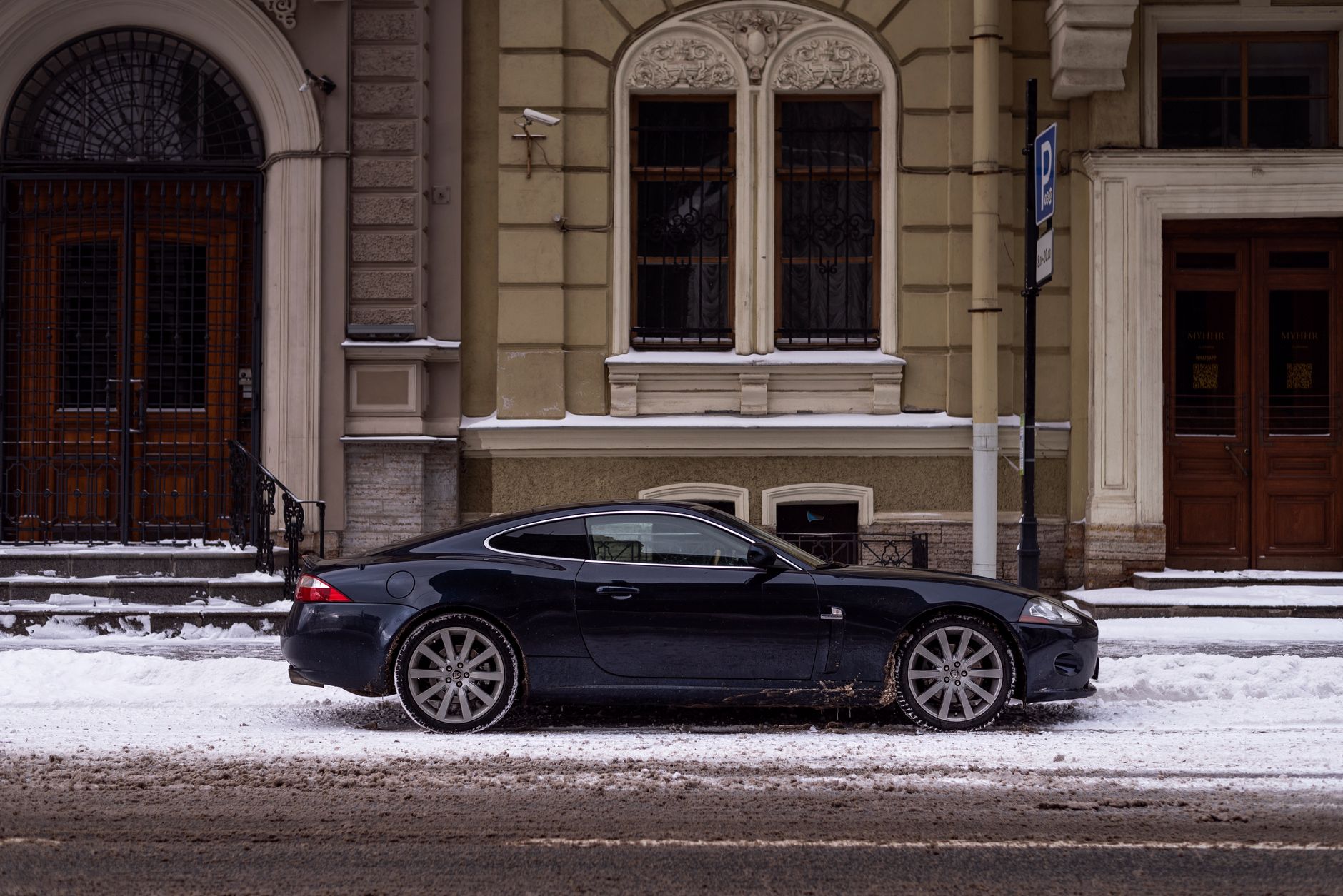 Czarny Jaguar XK zaparkowany zimą przy klasycznej kamienicy