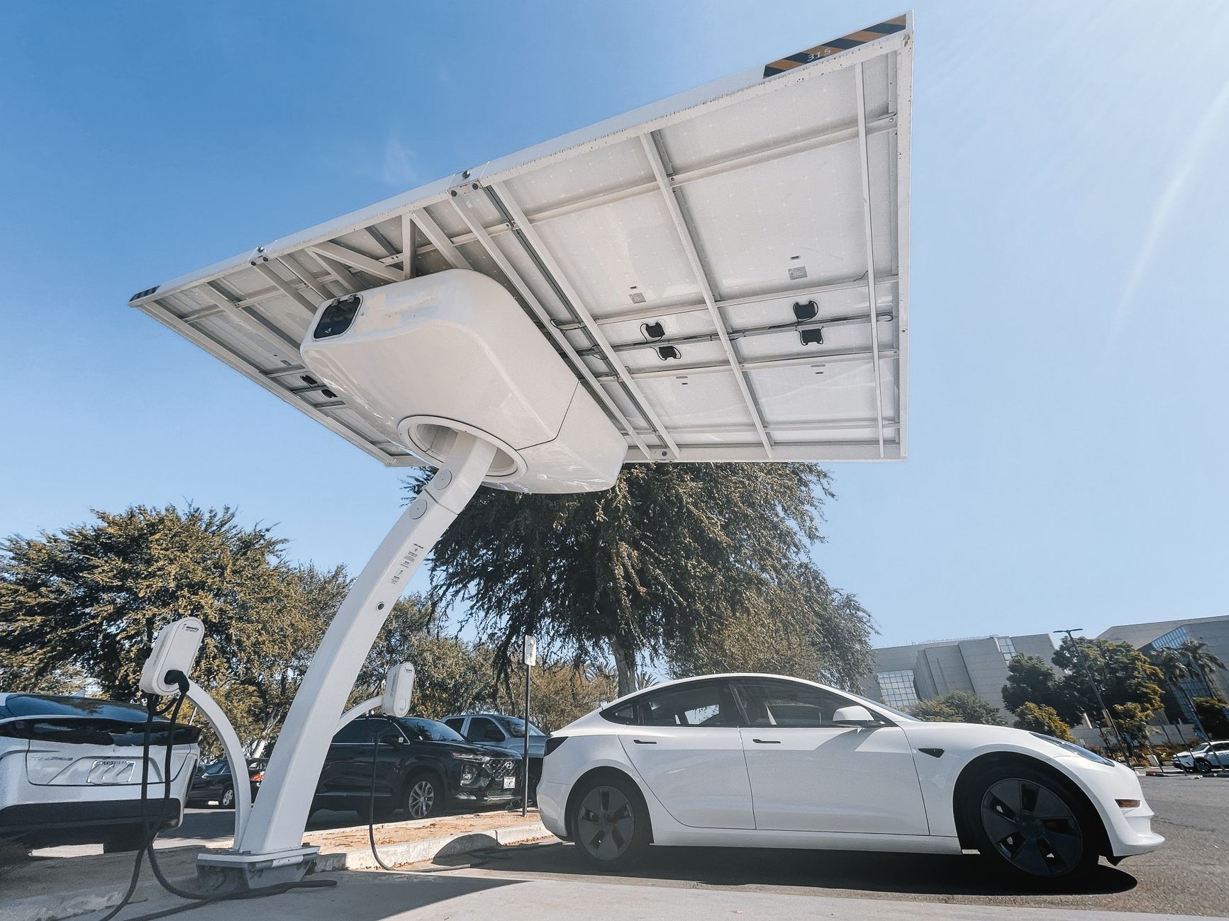 Elektryczne auto Tesla ładowane pod wiatą z panelami fotowoltaicznymi
