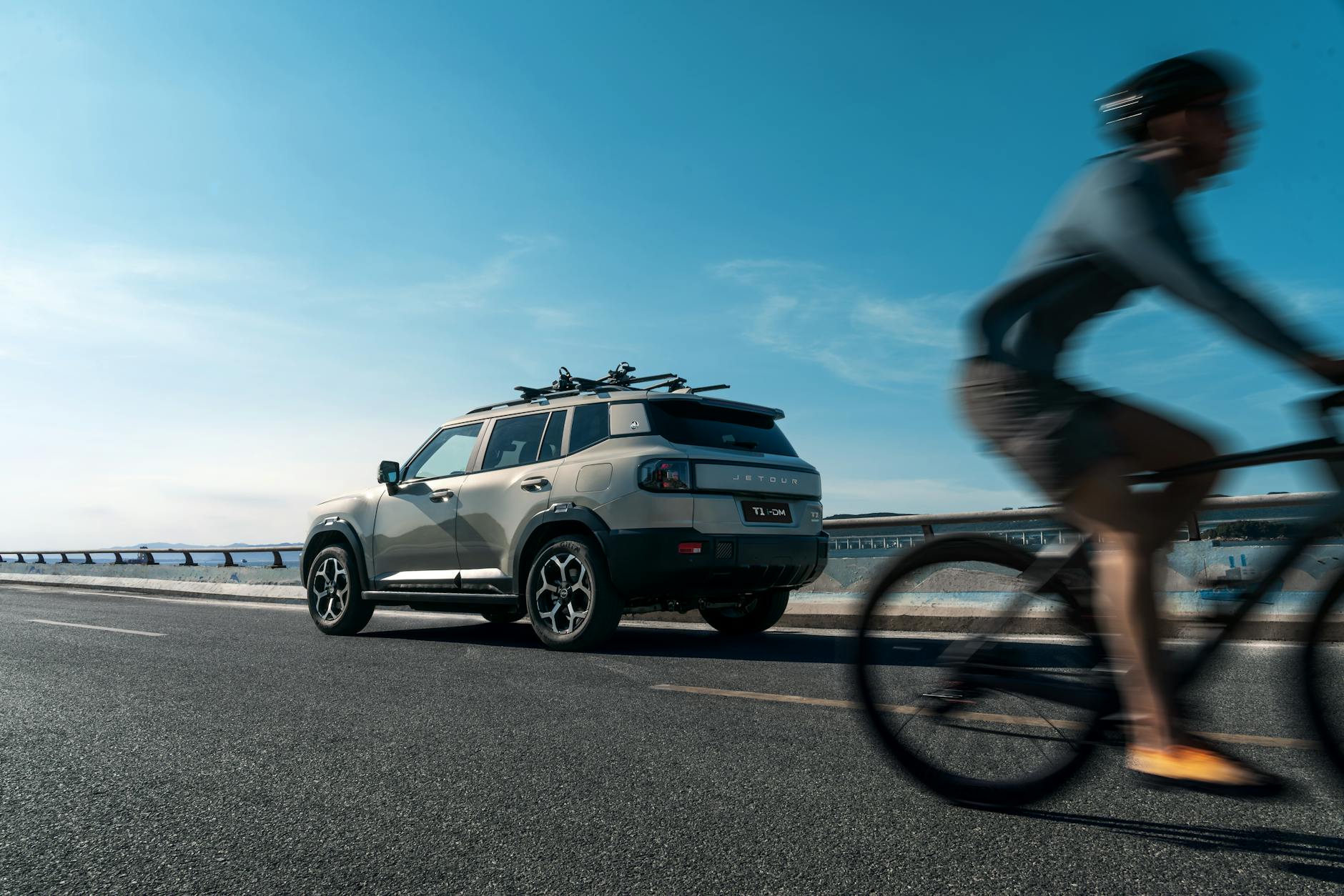 SUV z bagażnikiem rowerowym mijany przez rowerzystę na słonecznej drodze