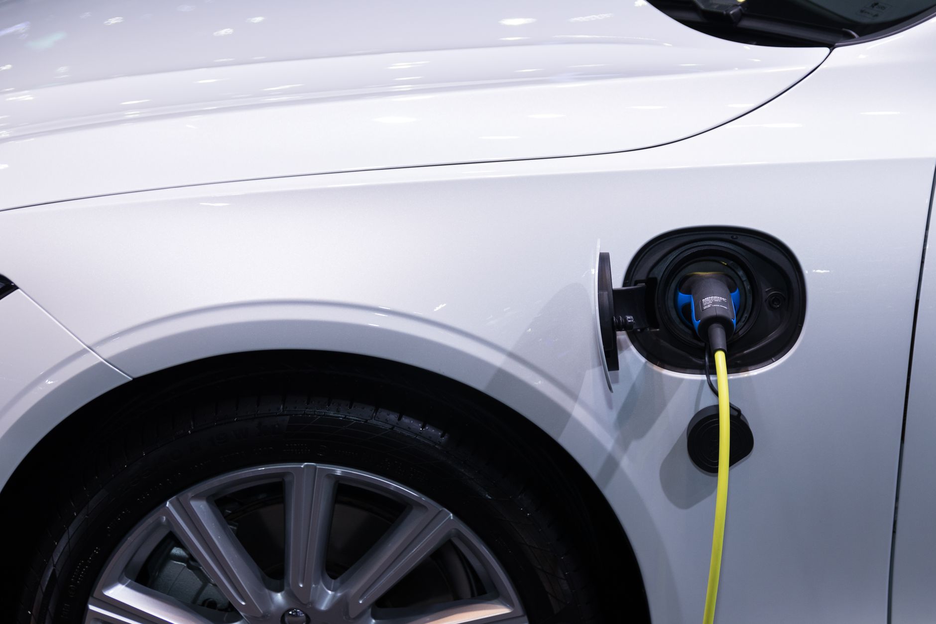 Zbliżenie na port ładowania białego auta elektrycznego podłączonego do ładowarki